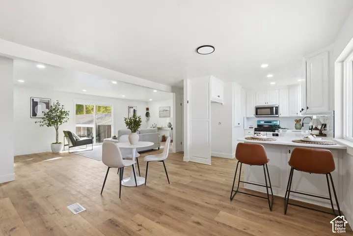 Open-concept living space featuring wood-finish flooring, recessed lighting, a kitchen with white cabinetry, stainless steel microwave, and white countertops
