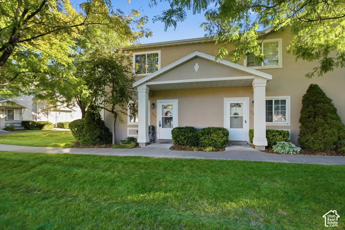 Stucco exterior with a covered entry, white frame windows, and mature trees