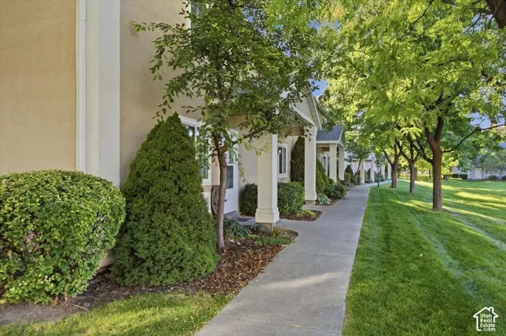 Concrete walkway bordered by manicured landscaping, mature trees, and stucco-finish building exteriors