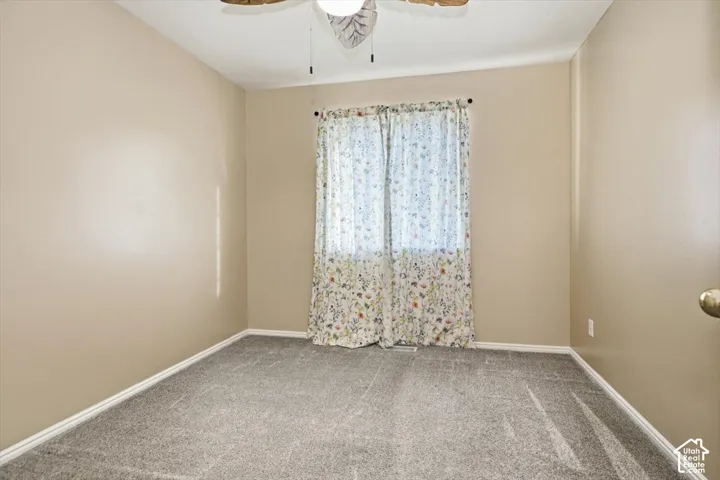 Neutral painted walls, grey carpeting, and a ceiling fan with light fixture