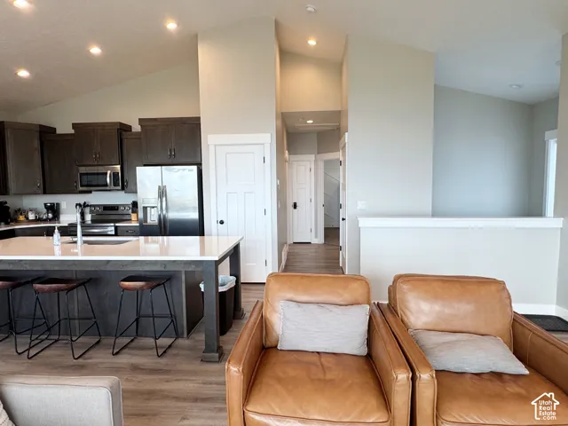 Open-concept living space with vaulted ceilings, recessed lighting, wood-finish flooring, a kitchen island with seating, and stainless steel appliances
