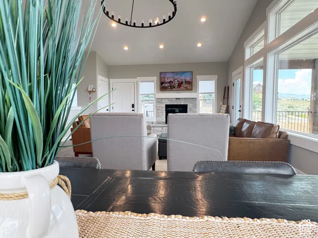Vaulted ceiling, recessed lighting, large windows, stone-clad fireplace, and a contemporary chandelier