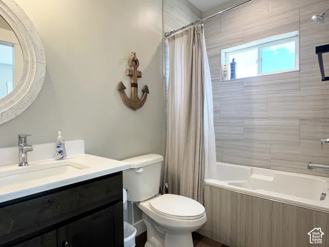 Bathroom featuring a dark wood-finish vanity with a white countertop and integrated sink, a white bathtub with light wood-finish paneling, and a tiled shower surround with a window
