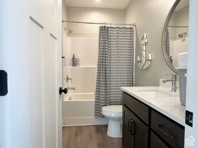 Wood-finish flooring with a white paneled door, a dark wood-finish vanity with a white countertop and integrated sink, a round mirror, and a white bathtub with a shower