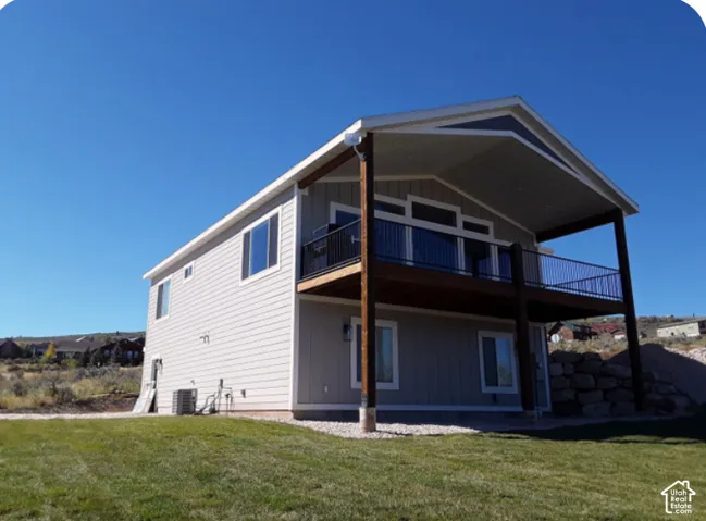 Two-story residence with light-colored siding, a covered upper-level deck with dark railing, and a ground-level patio