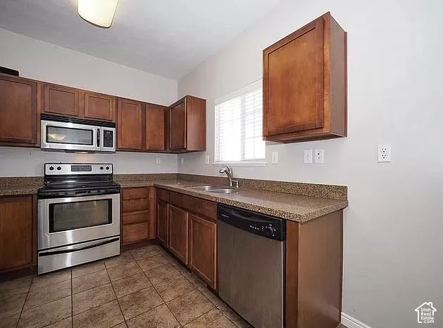 Kitchen featuring wood-finish cabinetry, stainless steel appliances, speckled countertops, and tiled flooring