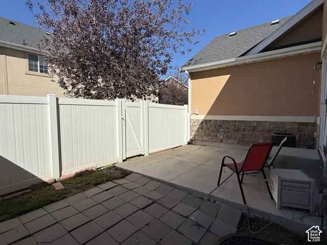 Paved patio featuring a stone veneer foundation, stucco exterior, and white privacy fencing with gate