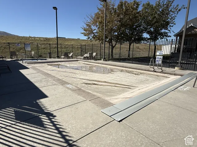 Concrete pool deck with covered swimming pool, adjacent hot tub, and black metal perimeter fencing