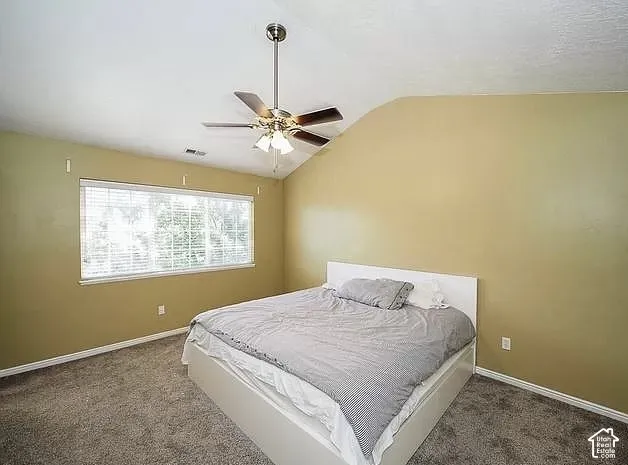 Sloped ceiling room featuring a ceiling fan with integrated lighting, a wide window with blinds, and carpet flooring