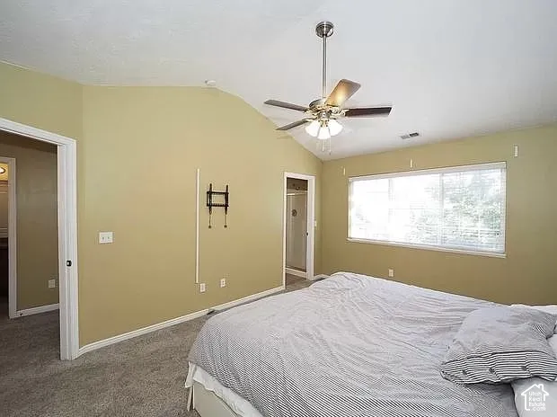 Vaulted ceiling with a ceiling fan, carpet flooring, a large window, and an attached full bathroom