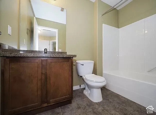 Wood-finish vanity with a stone-finish countertop, full-width mirror, white toilet, and a white tub with shower surround