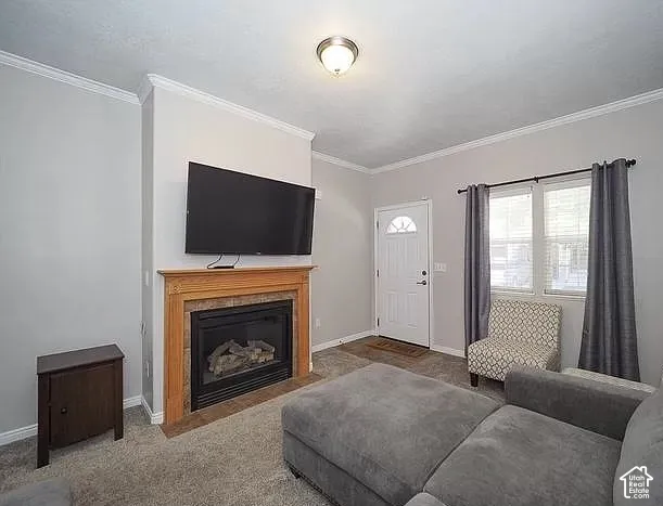 Living area featuring a gas fireplace with a wood-finish mantel and stone surround, crown molding, and neutral-toned carpeting