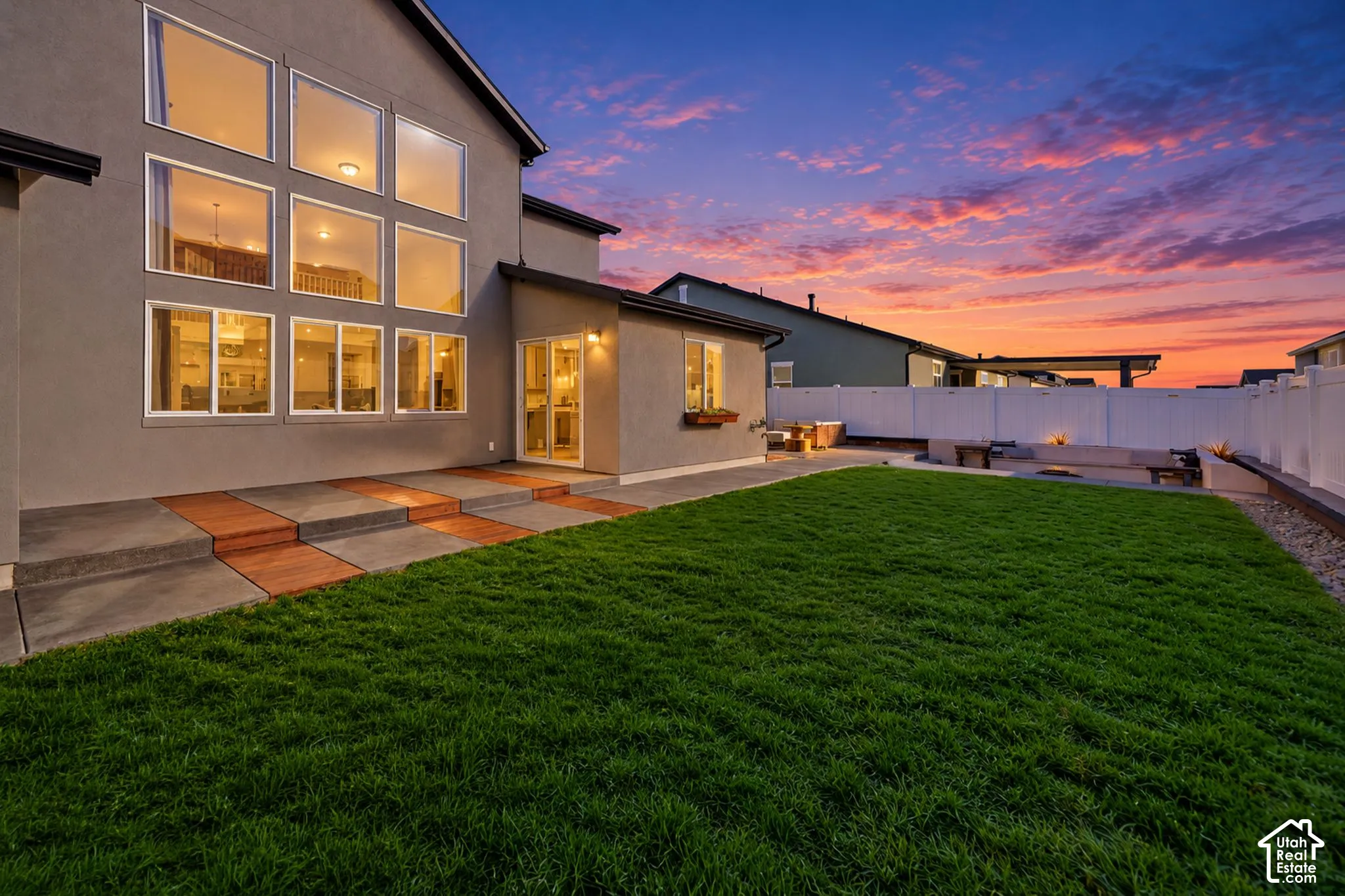 Expansive backyard featuring a manicured lawn, an extended patio with integrated steps, and a built-in fire pit with seating