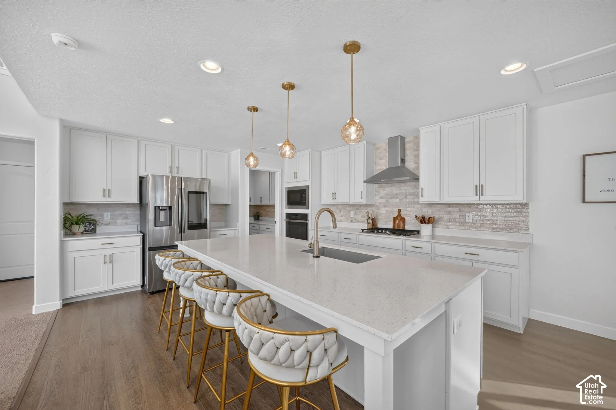 Spacious kitchen featuring white cabinetry, a large center island with a sink, stainless steel appliances, and wood-finish flooring