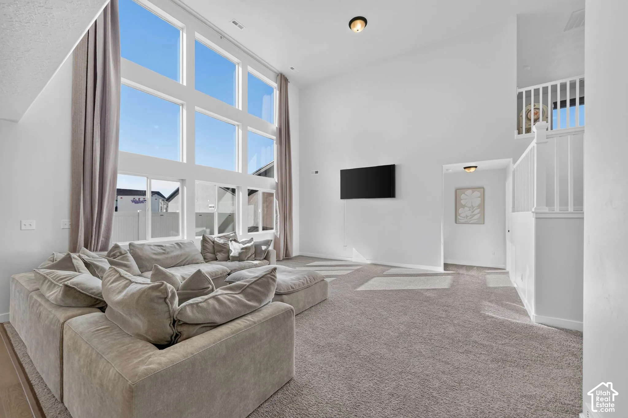 Two-story window wall, high ceilings, white painted walls, light gray carpet, and white staircase railing