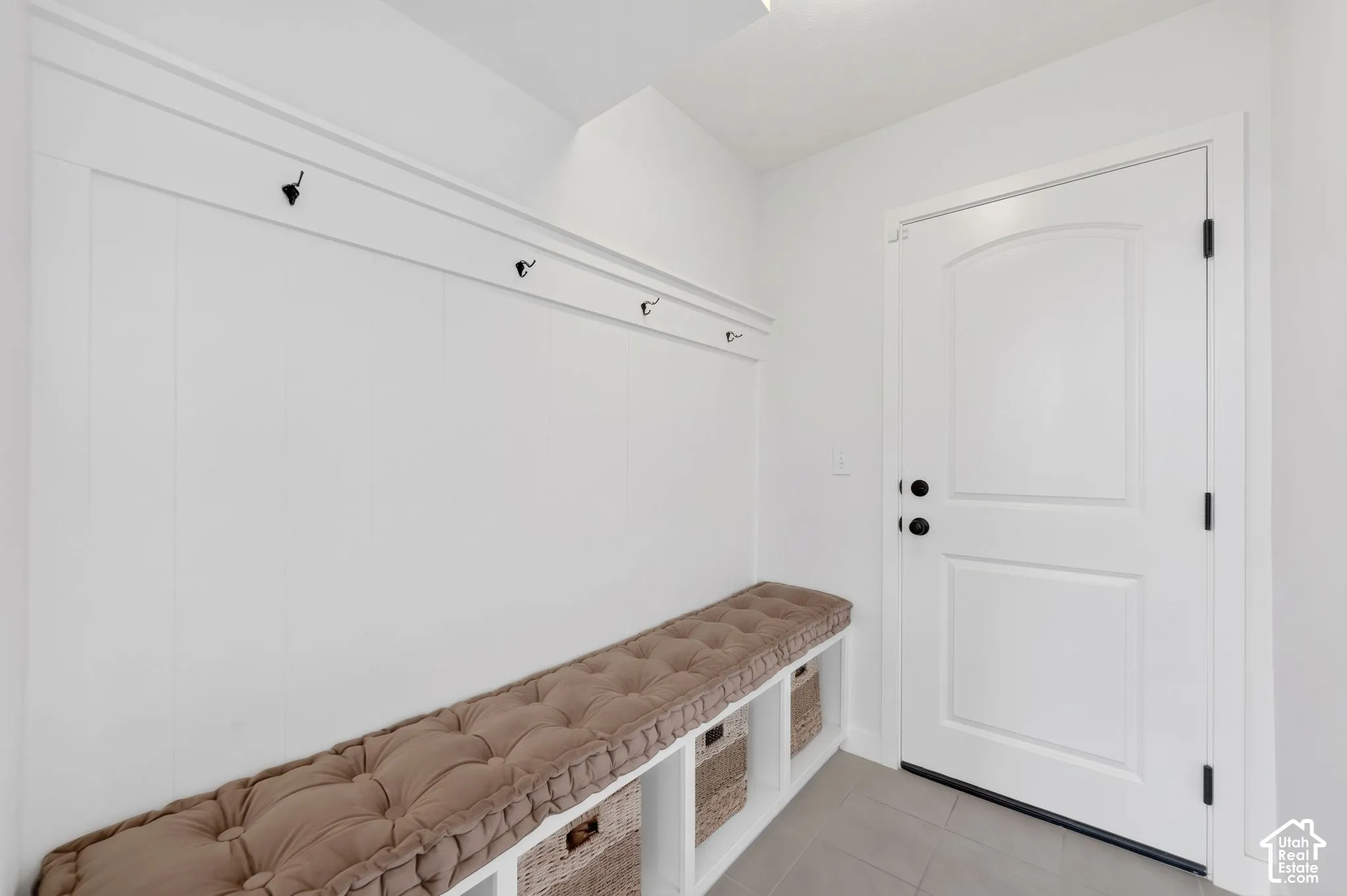 Built-in bench with integrated storage cubbies, wainscoting with coat hooks, and a paneled entry door with black hardware
