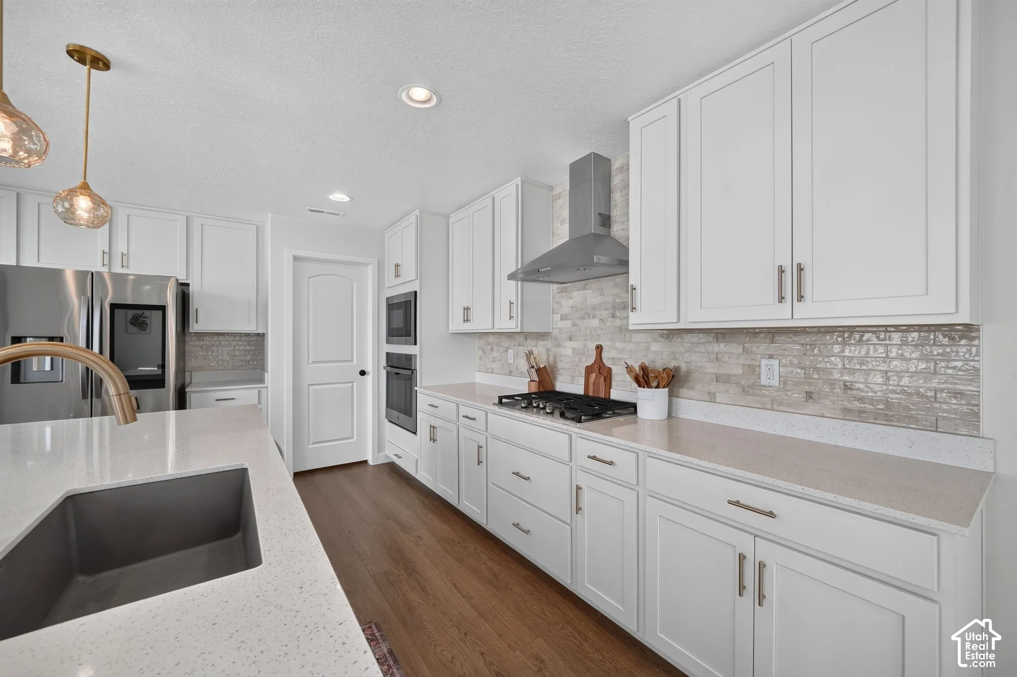 Kitchen featuring white shaker-style cabinetry, stainless steel appliances, stone countertops, a subway tile backsplash, and wood-finish flooring