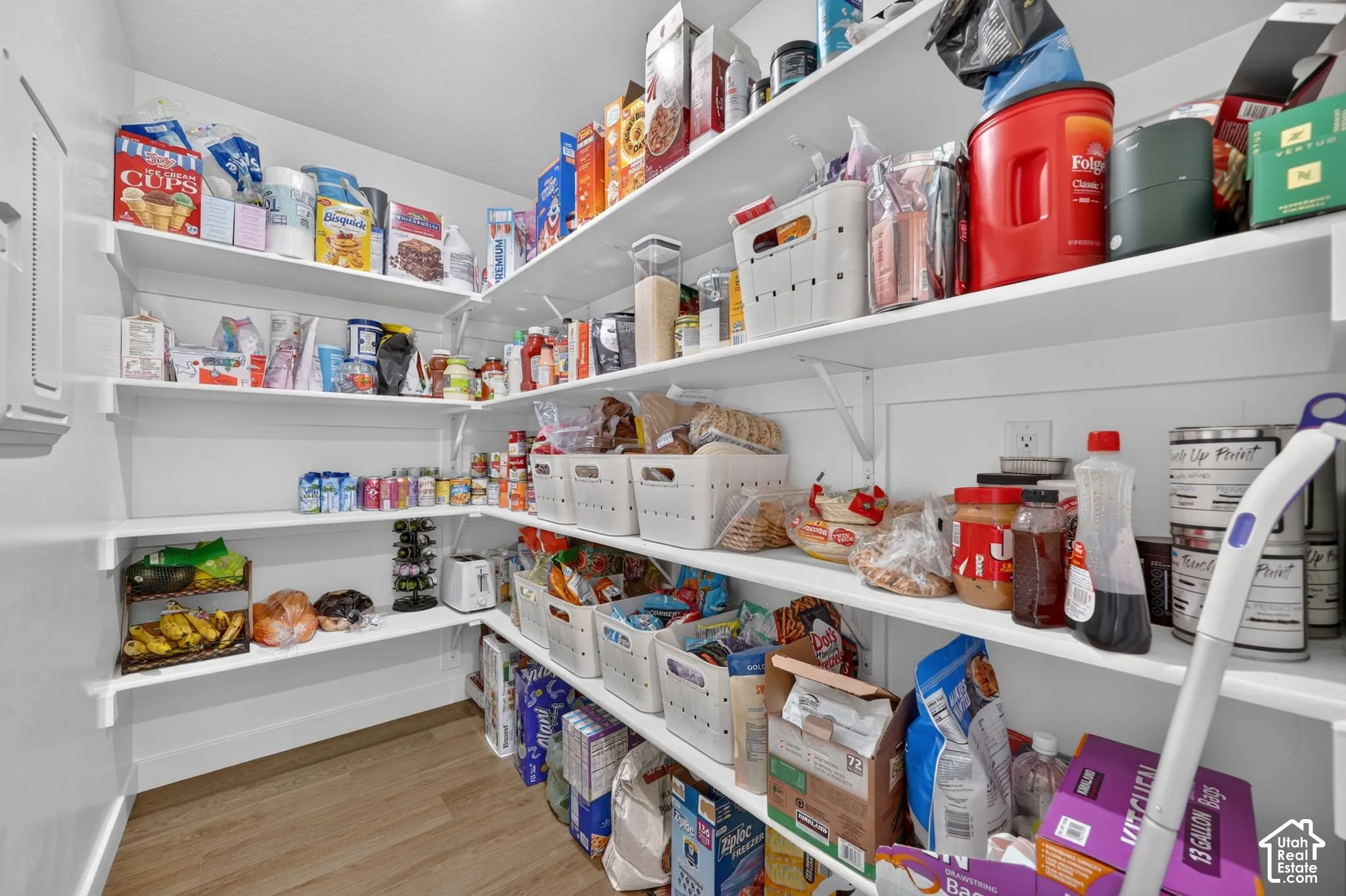Spacious pantry featuring floor-to-ceiling white cabinetry with multiple shelves, wood-finish flooring, and ample storage capacity for dry goods, beverages, and household supplies