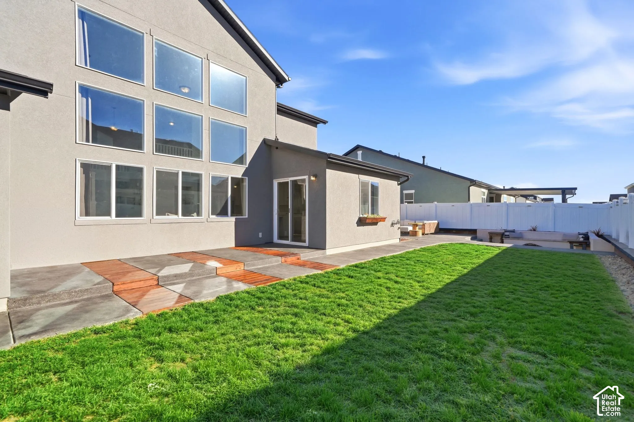 Stucco exterior with extensive window array, concrete patio with integrated wood-finish accents, and a manicured lawn