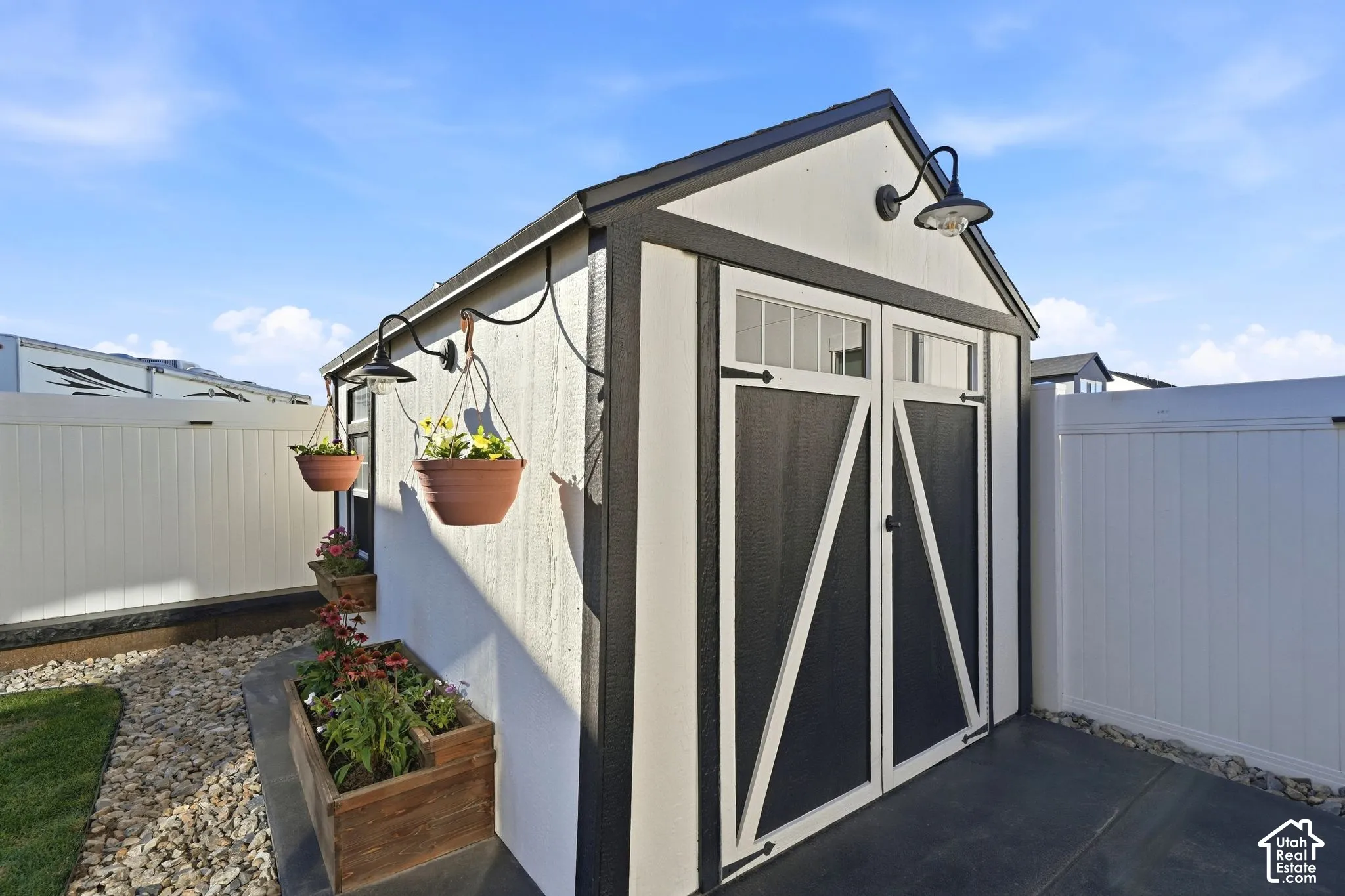 Detached shed with barn-style doors, overhead lighting, and an adjacent privacy fence