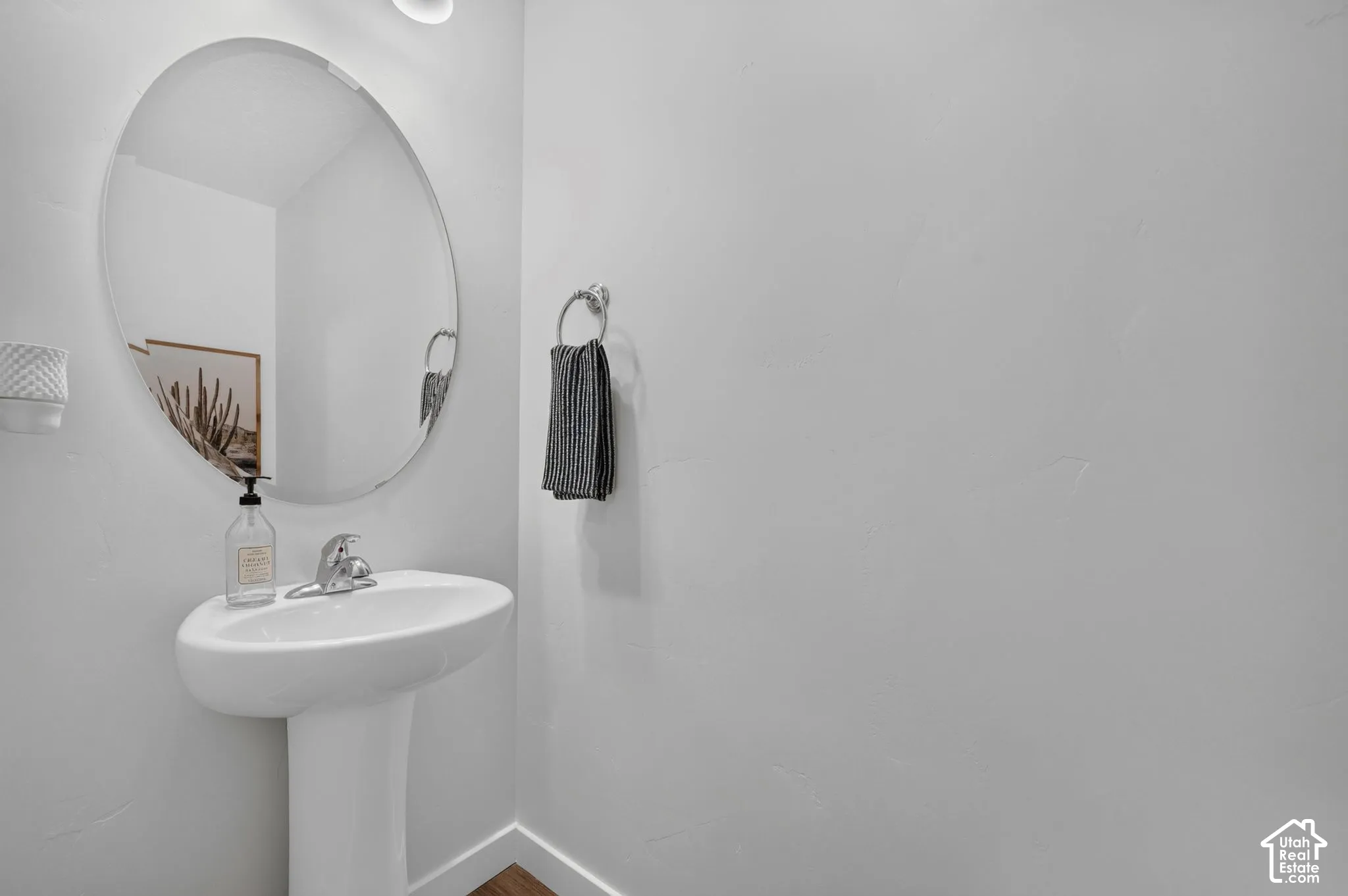 Pedestal sink with a chrome faucet, oval mirror, and overhead lighting