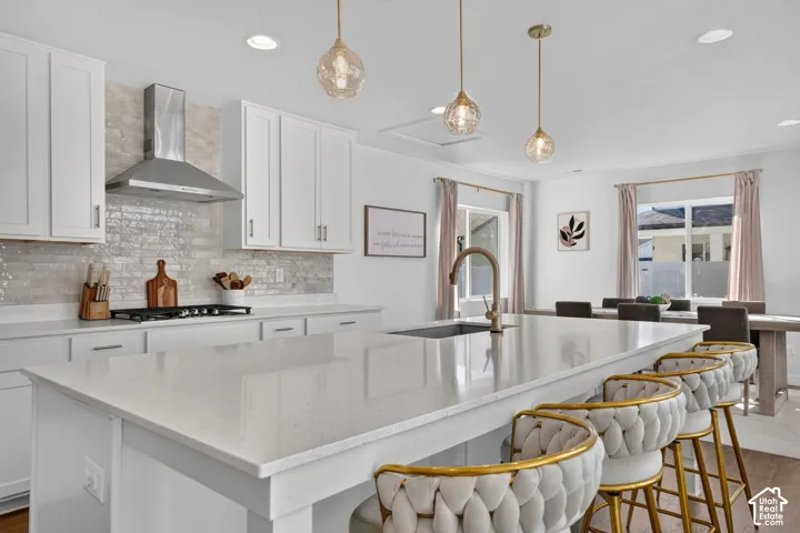 Expansive kitchen island with a built-in sink, white cabinetry, stainless steel range hood, and pendant lighting