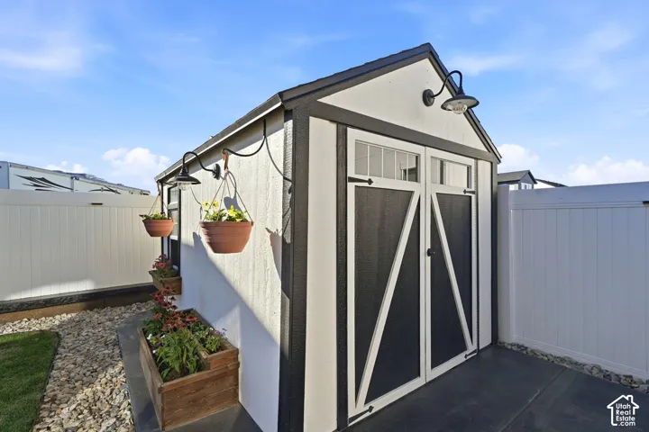 Detached shed with barn-style doors, overhead lighting, and an adjacent privacy fence