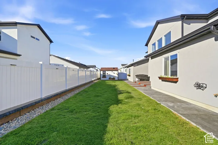 Expansive grassy yard with a white privacy fence, concrete pathway, and decorative window boxes