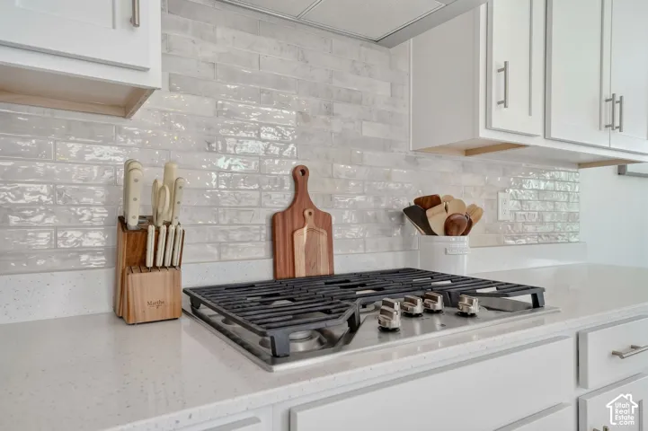 Built-in gas cooktop with grates, light-toned countertops, white subway tile backsplash, and white cabinetry with brushed nickel pulls