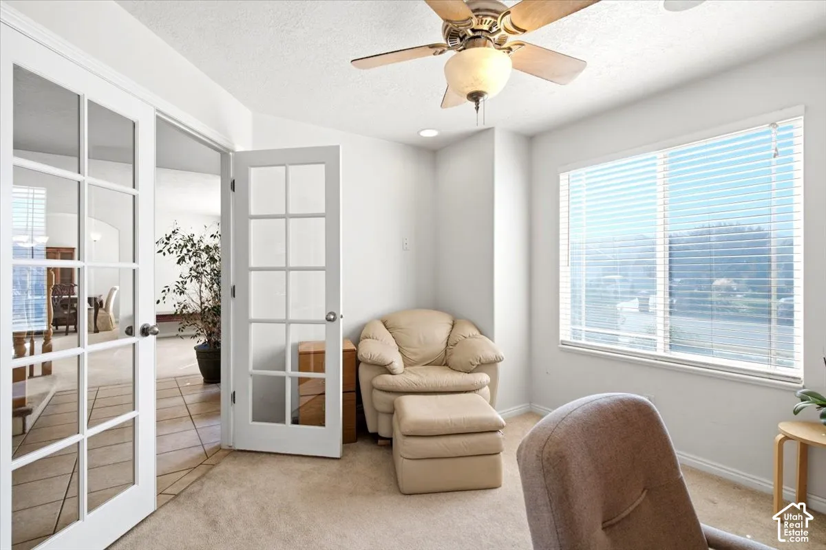 Light-filled room featuring a ceiling fan with integrated lighting, large window with blinds, and double French doors with glass panes