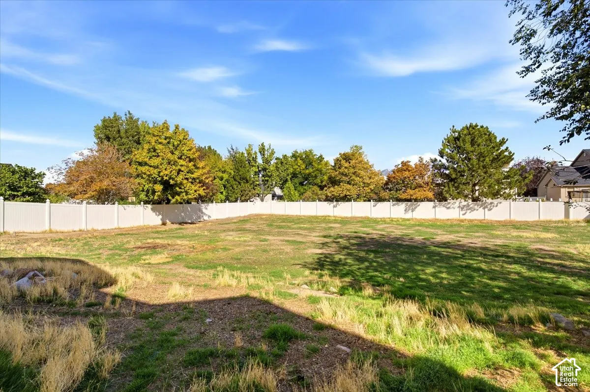 Expansive outdoor space featuring a white privacy fence and a variety of mature trees bordering the property