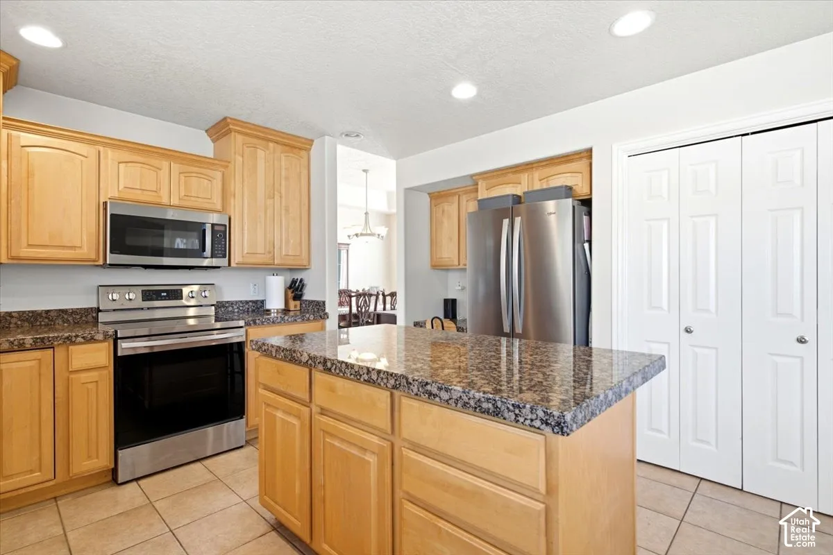 Kitchen featuring wood cabinetry, granite countertops, stainless steel appliances, a center island, and tiled flooring