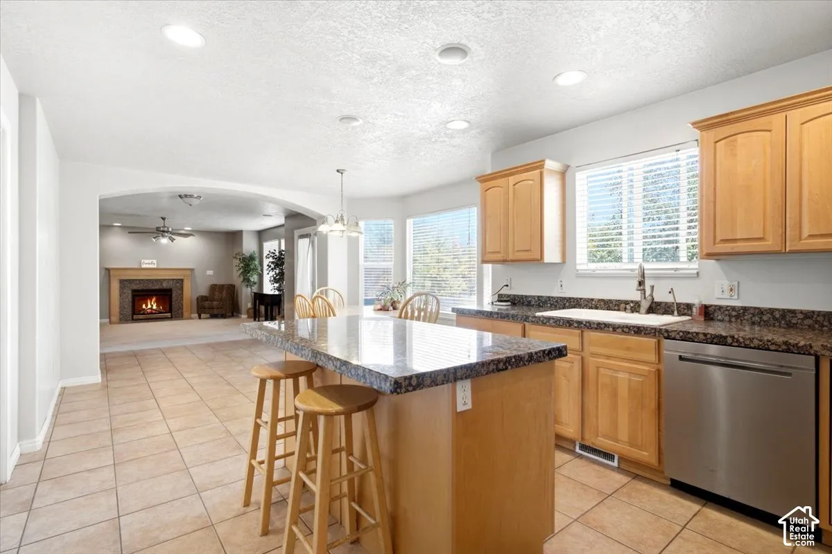 Kitchen with tile flooring, wood cabinetry, stone-finish countertops, and stainless steel dishwasher