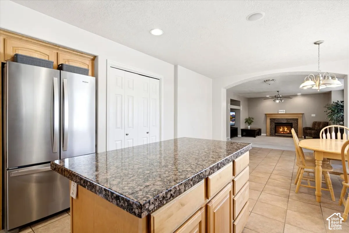 Kitchen island with a granite-style countertop, stainless steel refrigerator, and tiled flooring