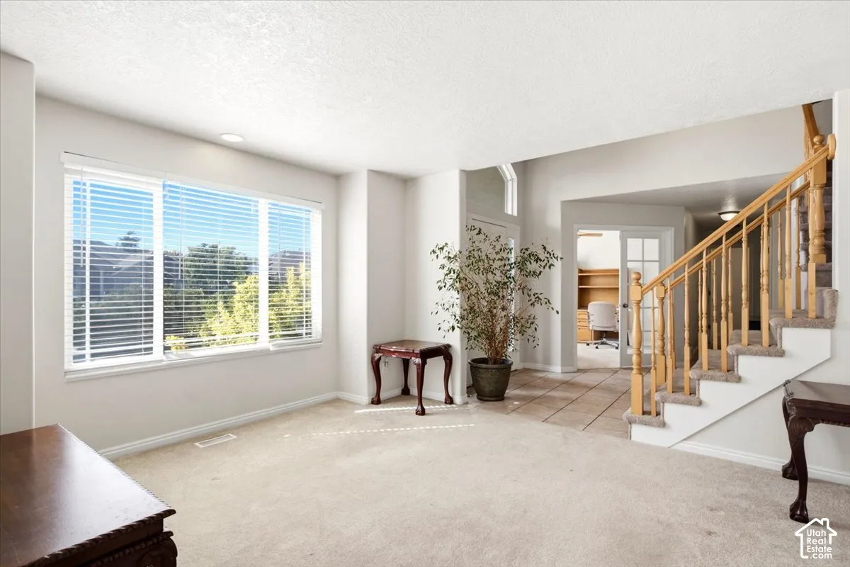 Expansive room with large windows, carpet flooring, a built-in staircase with wood railing, and a tiled entry