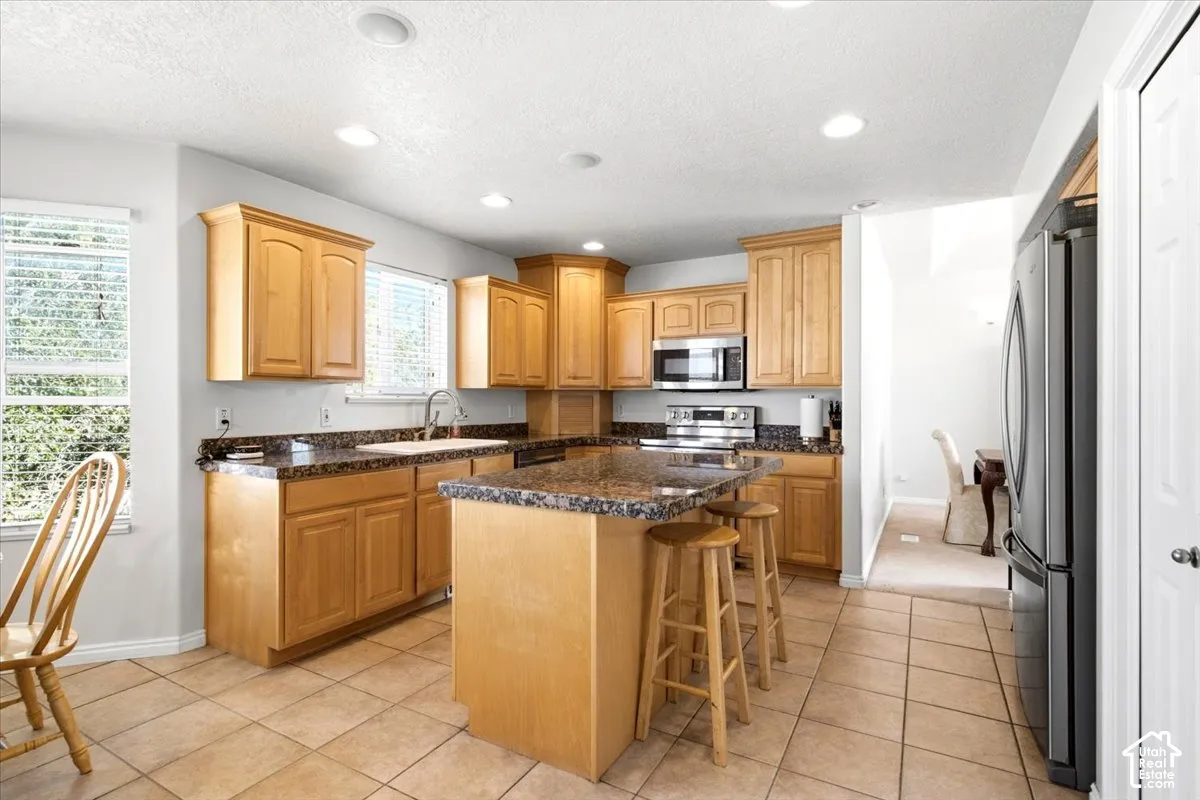Kitchen featuring wood cabinetry, integrated stainless steel appliances, speckled stone countertops, and tile flooring