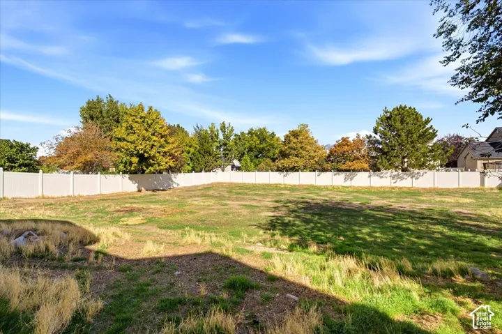 Expansive outdoor space featuring a white privacy fence and a variety of mature trees bordering the property