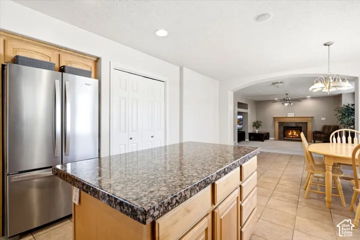 Kitchen island with a granite-style countertop, stainless steel refrigerator, and tiled flooring