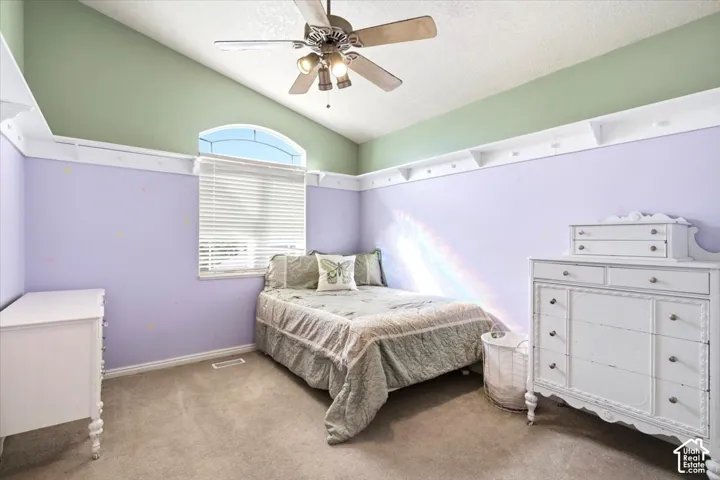 Vaulted ceiling with a ceiling fan, arched window, wall-mounted shelving, window blinds, and carpeted flooring