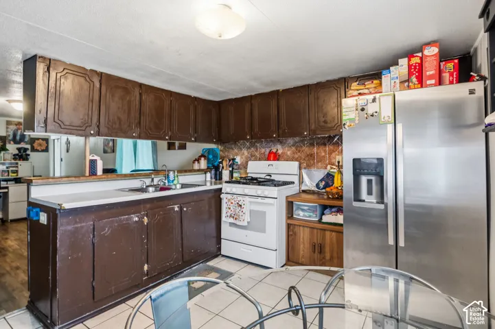 Kitchen featuring upper and lower cabinetry, a double basin sink, a white oven/stove combination, and a stainless steel refrigerator