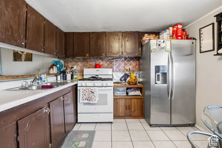 Kitchen featuring white tile flooring, brown cabinetry, a stainless steel refrigerator, and a white gas range