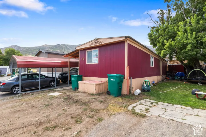 Red exterior siding with tan trim, a two-car carport, a paved walkway, and a grassy side yard with mature trees