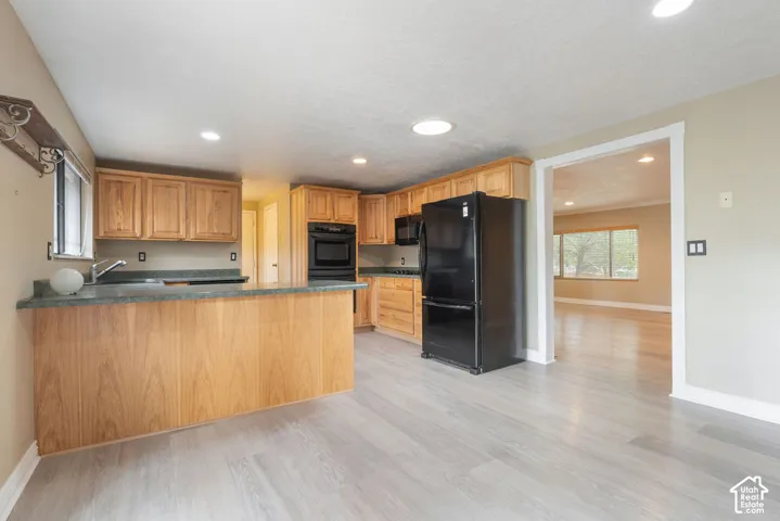 Kitchen featuring light wood cabinetry, a built-in oven, black appliances, and light grey wood-finish flooring