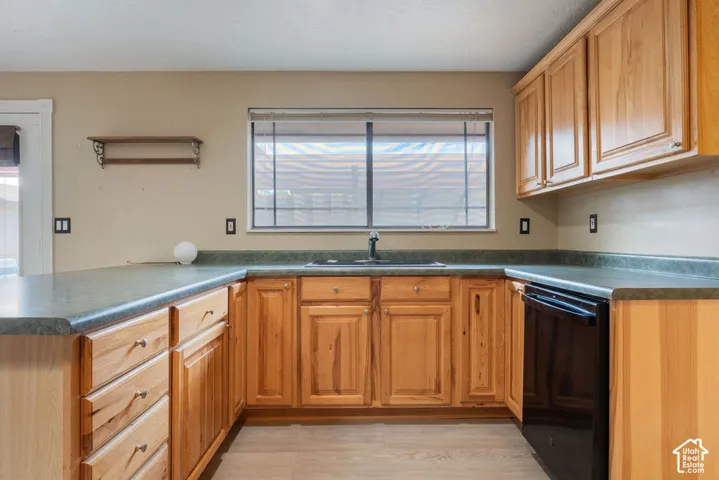 U-shaped kitchen featuring wood-finish cabinetry, dark countertops, a stainless steel sink with a black faucet, a black dishwasher, and wood-finish flooring