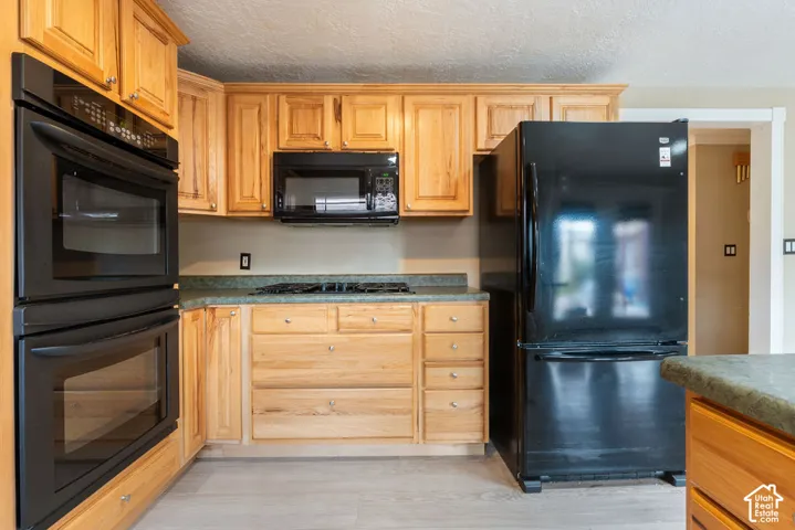 Kitchen featuring wood cabinetry, built-in double ovens, a gas cooktop, black appliances, and durable countertops