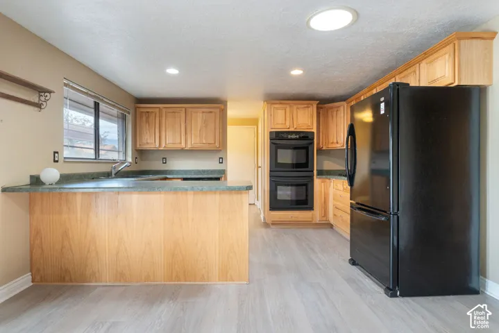 Kitchen featuring light wood-finish cabinetry, black double wall ovens, a black refrigerator, green countertops, and wood-finish flooring