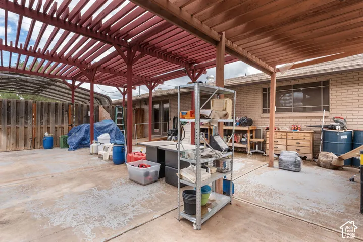 Expansive concrete patio area with a wooden pergola, brick exterior, and privacy fencing