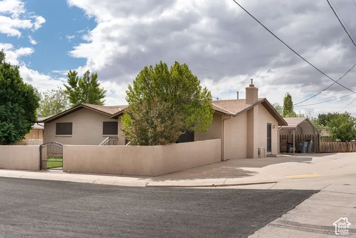 Brick exterior with a peaked roofline, chimney, and a stucco privacy wall featuring an ornamental metal gate