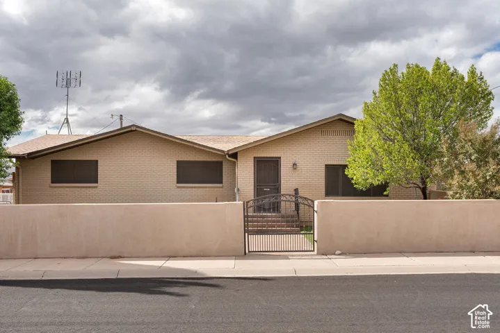 Brick exterior with a peaked roofline, featuring a stucco-finished privacy wall and an ornate metal gate
