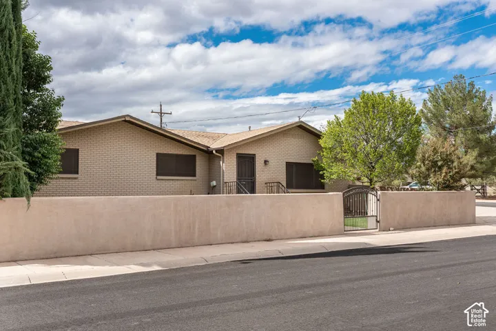 Light brick exterior featuring a stucco perimeter wall, wrought iron gate, and mature trees
